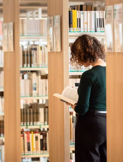 Une femme lisant un livre entre les étagères d'une bibliothèque.