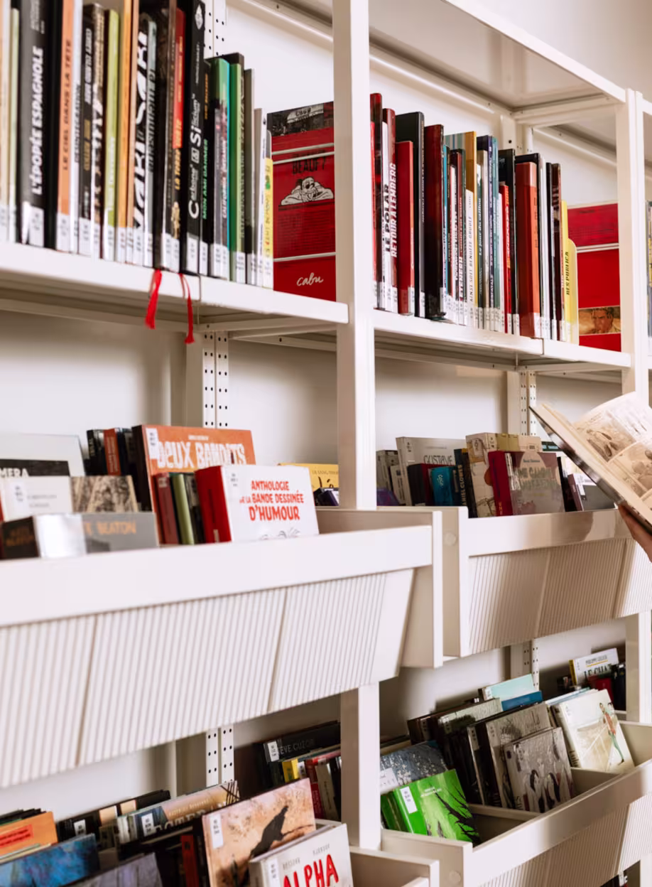 Jeune femme consultant une bande dessinée devant une bibliothèque blanche.